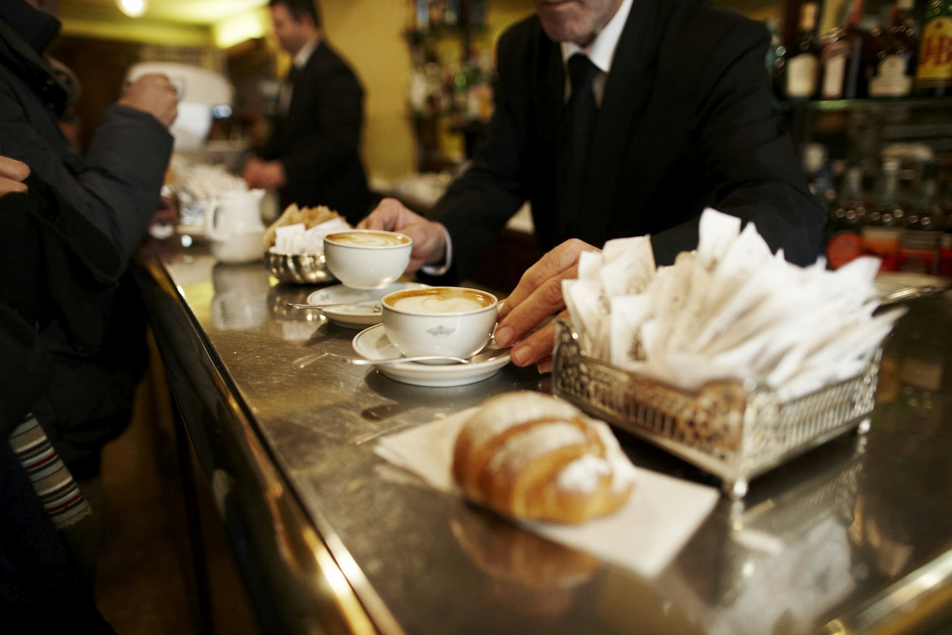 Close up of a capuccino and a flaky pastry on a wooden bar in Milan, Italy