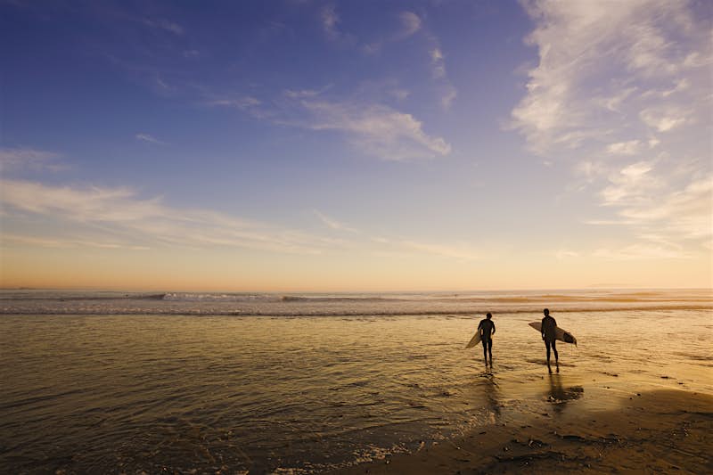 Features - USA, California, Ventura, two surfers entering sea, sunset, rear view Ttwo surfers entering sea, at sunset and low tide. The surfers are silhouetted against the calm water.