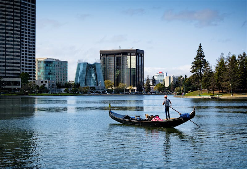 Features - Gondola on Lake Merritt Gondola cruises across a glass lake with the Oakland skyline in the background