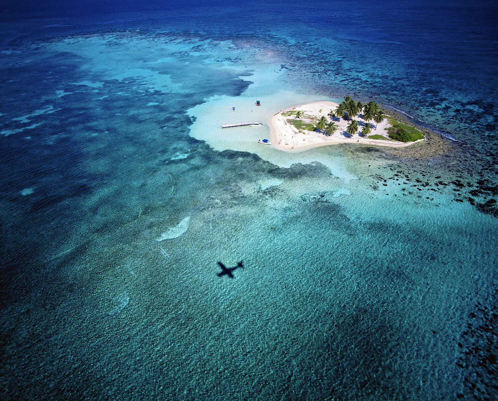 Features - Belize, Caribbean, Coral Reef, Goff's Cay A plane flies over Goff's Caye Island in Belize © Slow Images / Getty Images