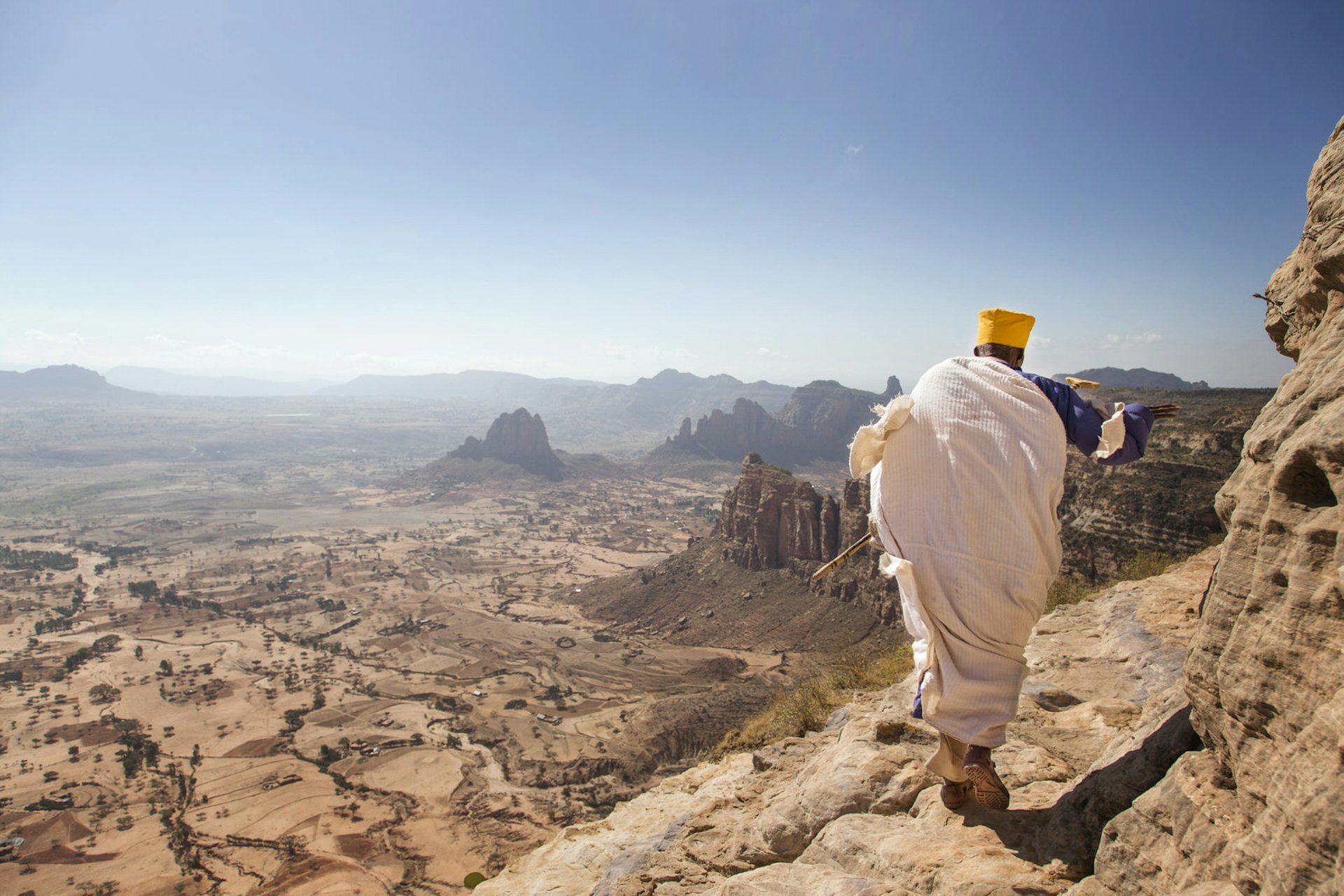 Priest walking along on ledge outside Abuna Yemata Guh cave church.