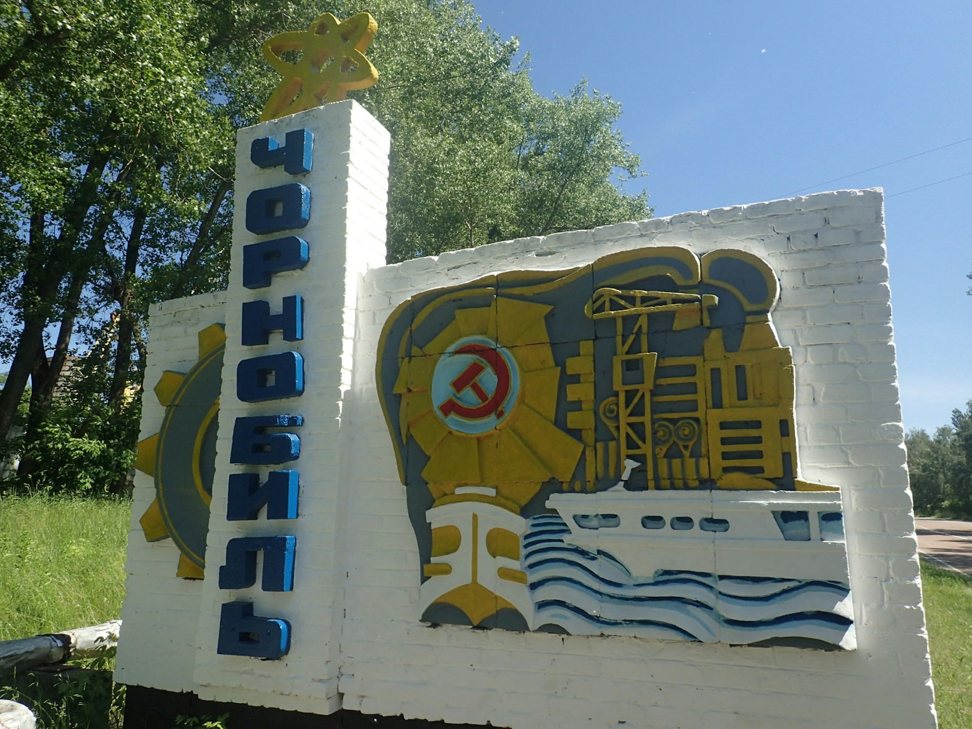 Soviet-era sign outside Chernobyl, with a depiction of the power plant in yellow on a white wall alongside blue script and a red hammer and sickle.