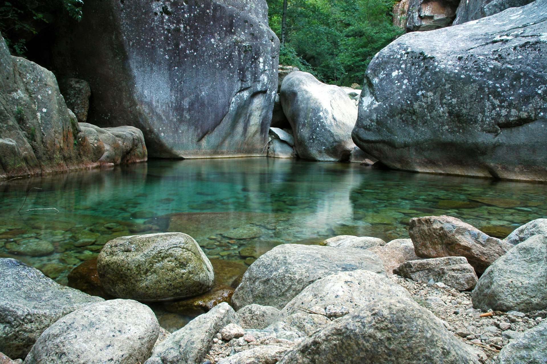 A clear pool of water surrounded by large grey boulders. 