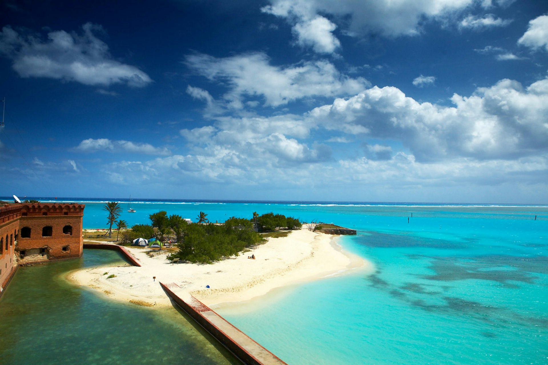 Brilliant blue seas surround a moat, which surrounds an old fort, with a sand bar in the foreground. National Parks: The best free things to do in the US parks