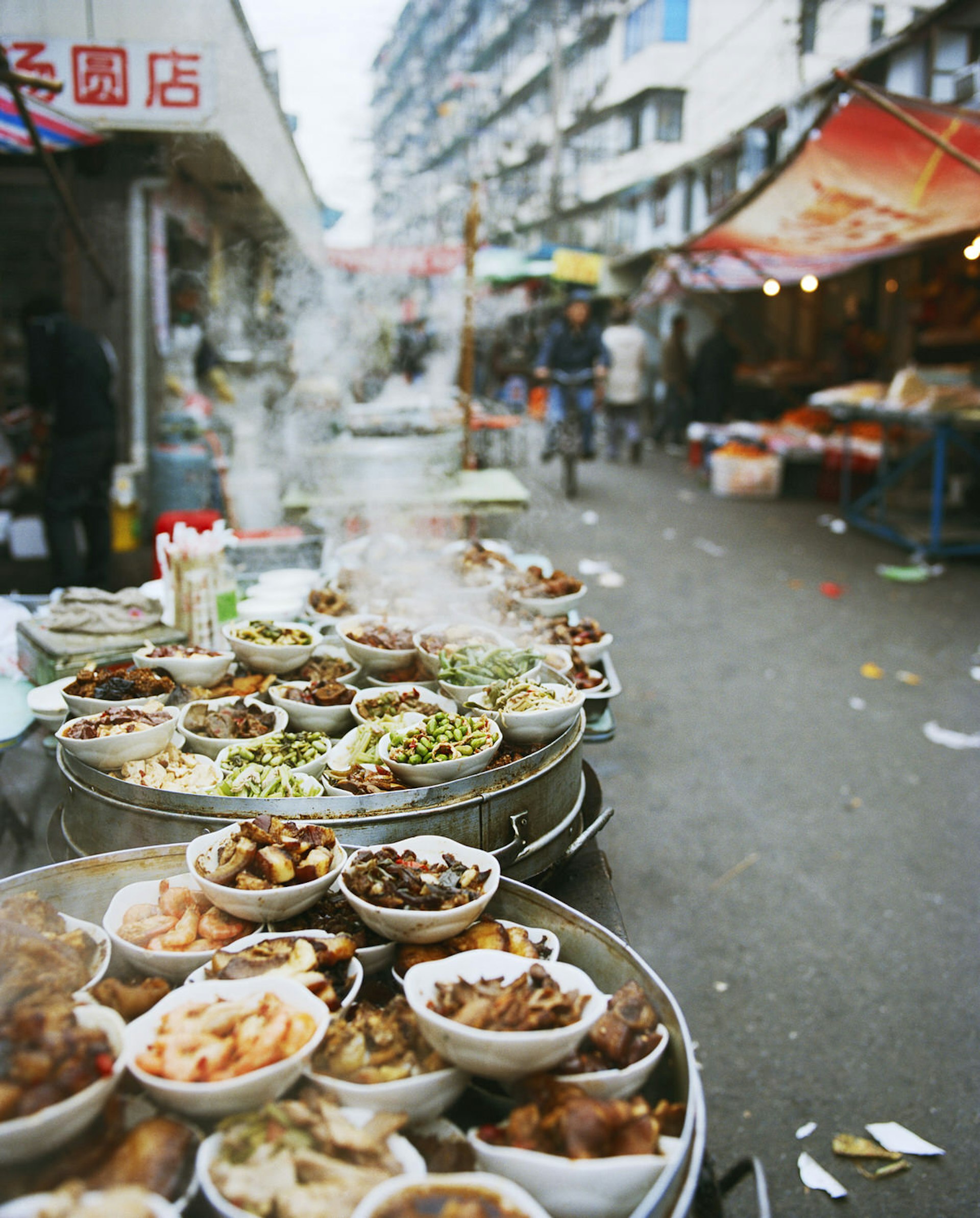 A series of small dishes at a food stand on Sipailou Street near Yu Gardens, Shanghai. The dishes include deep-fried shrimp, red-braised pork, and fava beans.