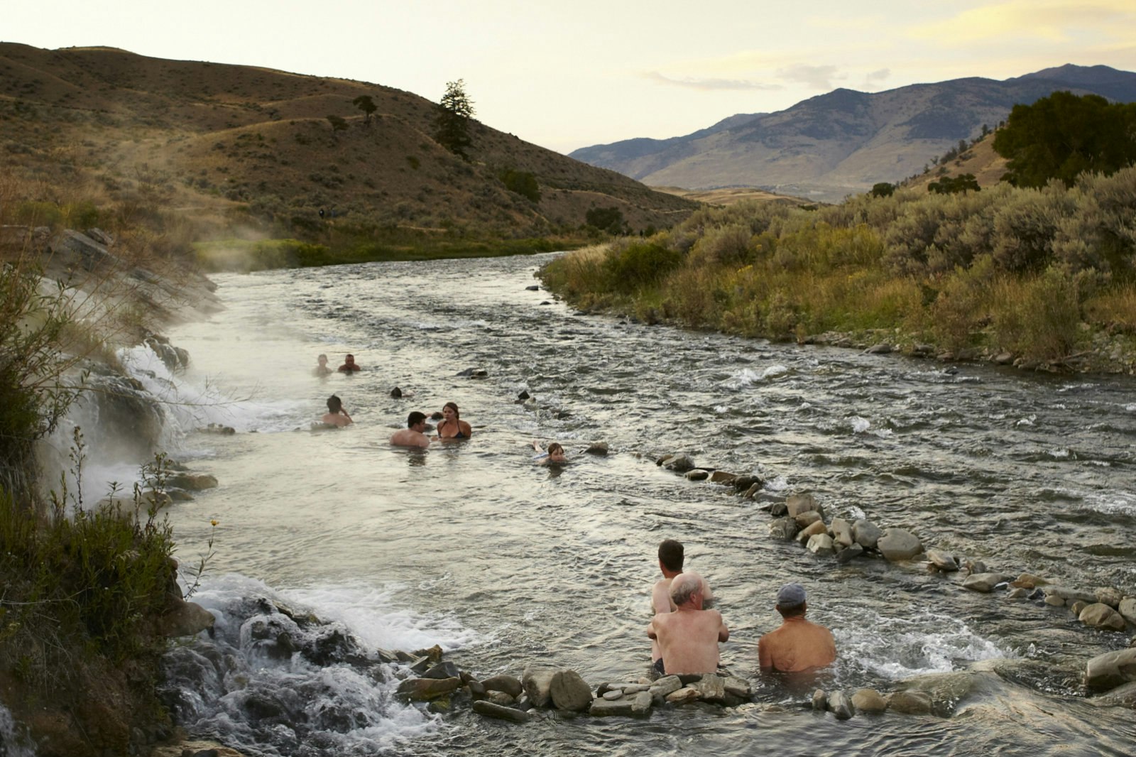 Steam rises from a river as about 15 people sit in the swiftly moving river. National Parks: The best free things to do in the US parks