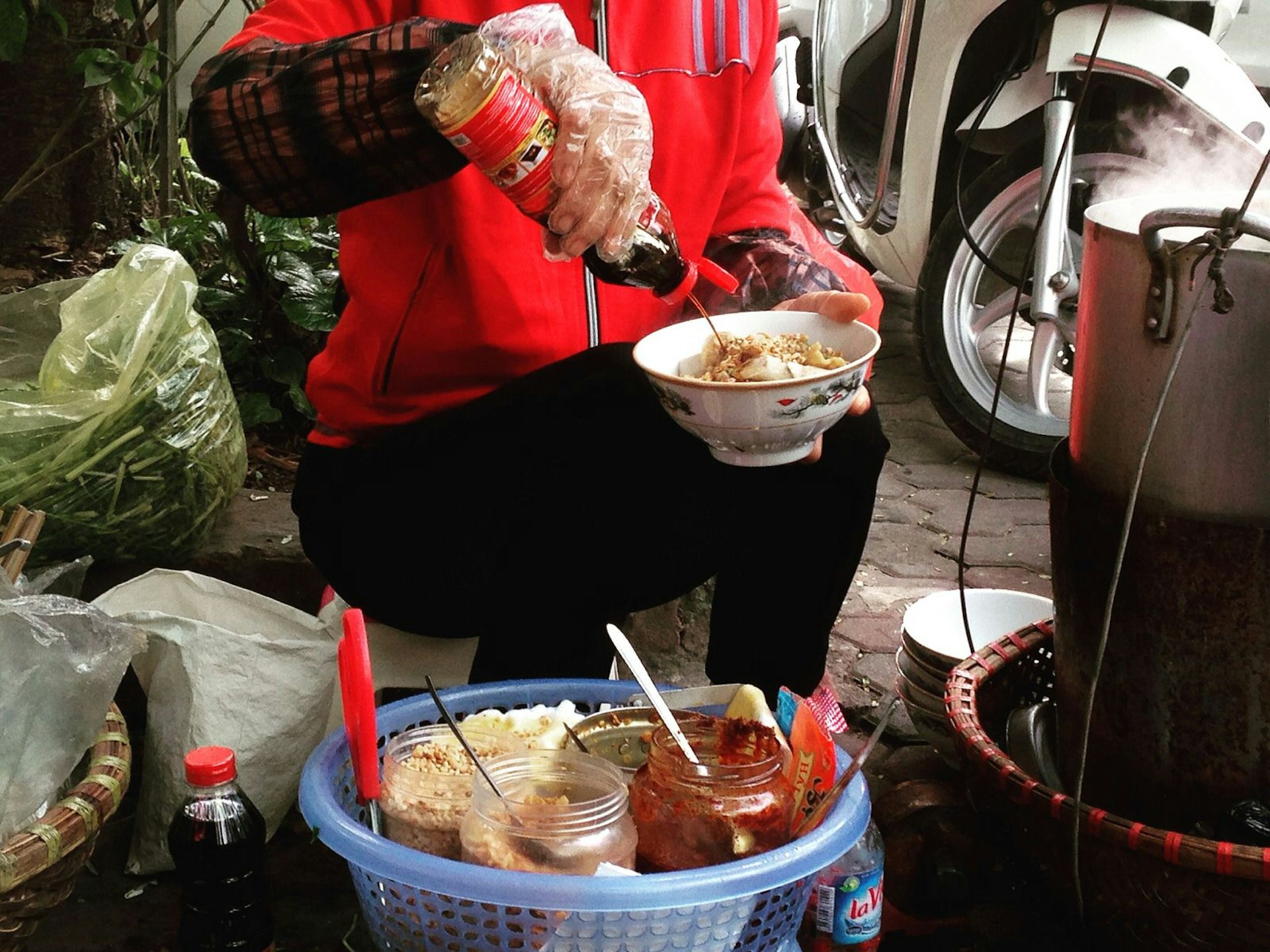 Street food vendor squirts sauce on a bowl of banh da tron 