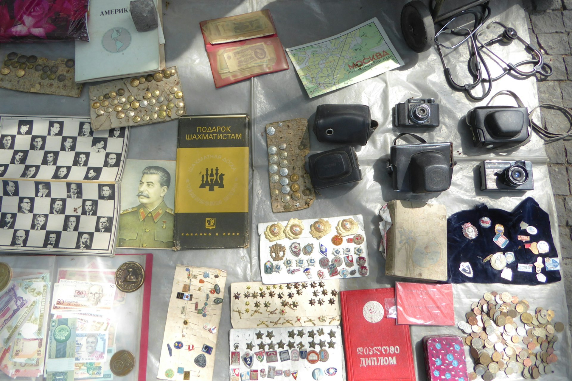Many different items lay out for sale on a mat at a market, including coins, badges and books from the Soviet era