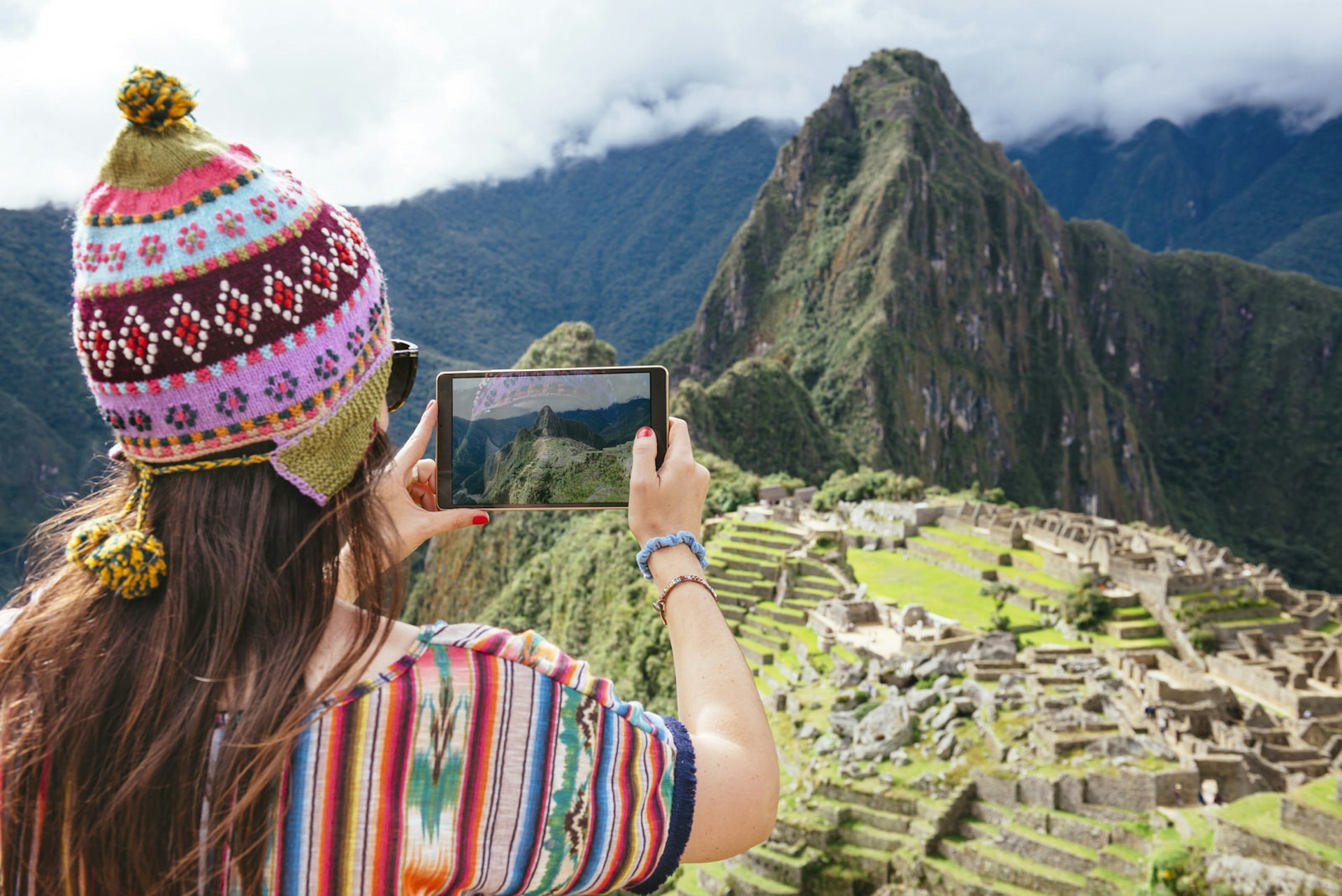 Peru, woman taking pictures of Machu Picchu citadel and Huayna Picchu mountain with a tablet