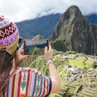 Features - Peru, woman taking pictures of Machu Picchu citadel and Huayna Picchu mountain with a tablet