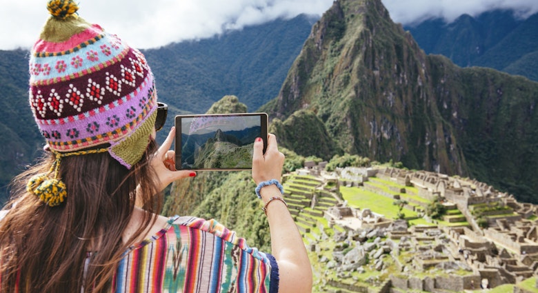 Features - Peru, woman taking pictures of Machu Picchu citadel and Huayna Picchu mountain with a tablet