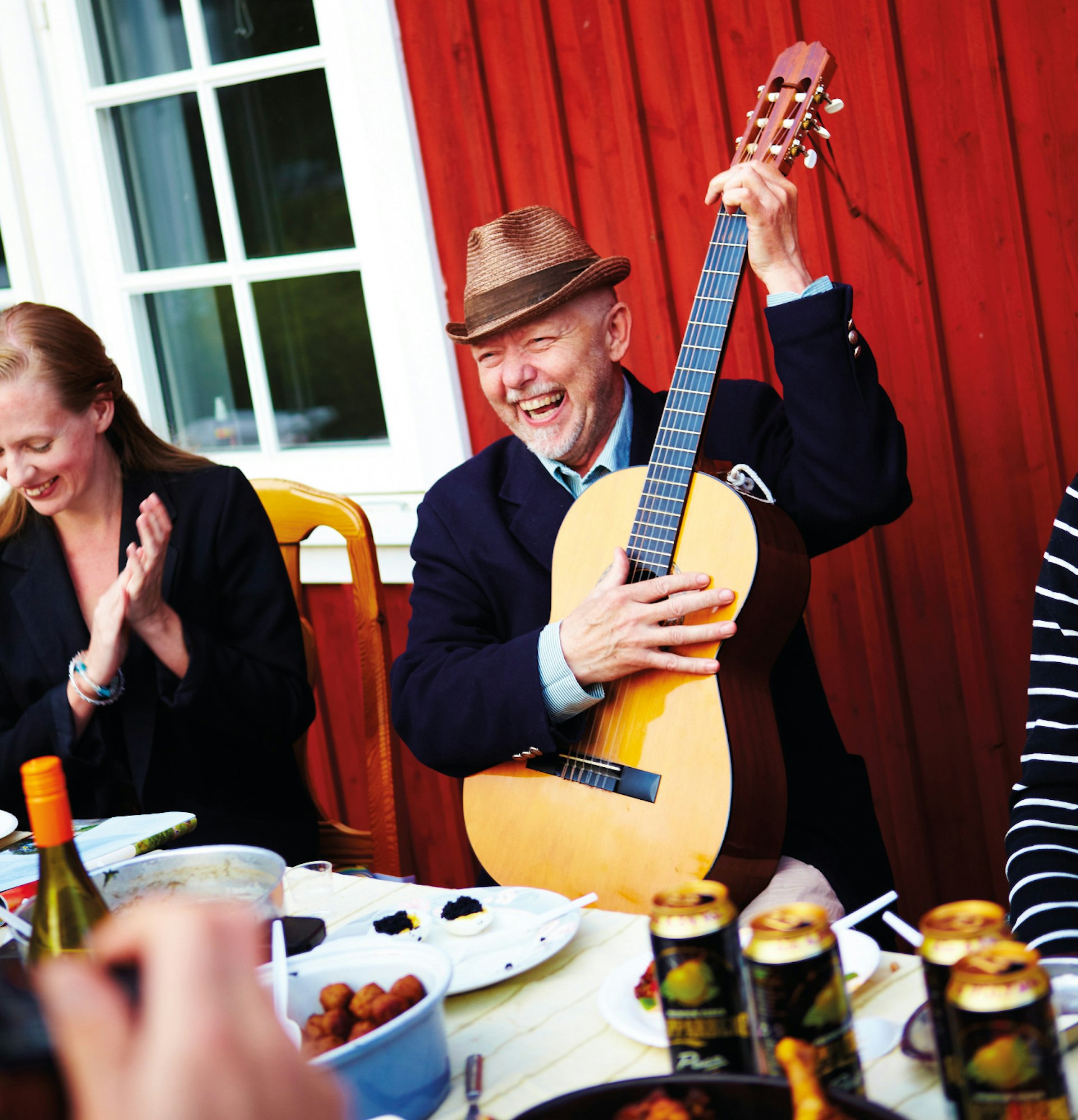 Man playing guitar at table during Midsummer celebrations.