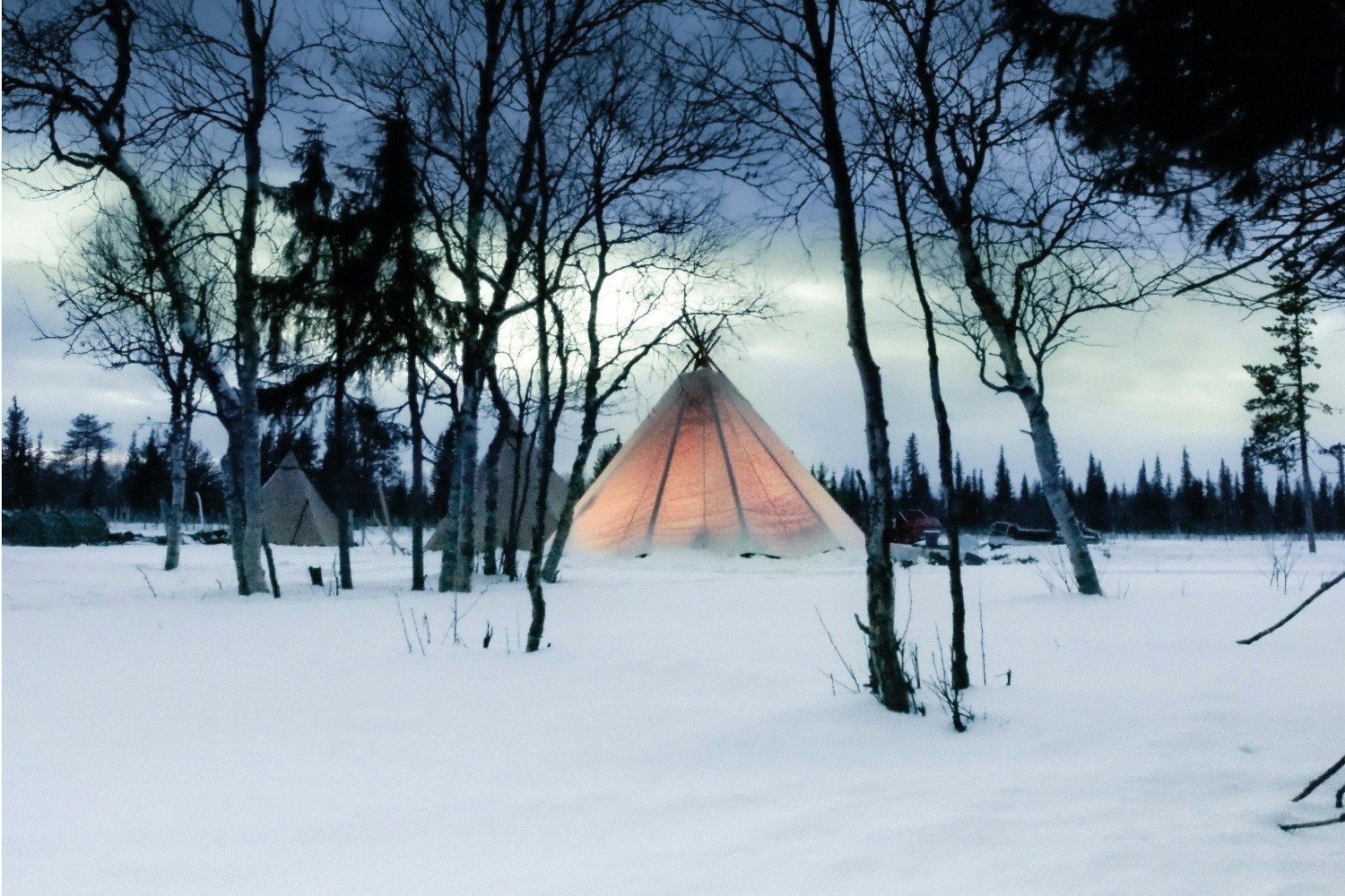 Glow of a traditional Sami tent (lavvu) in snow covered forest.