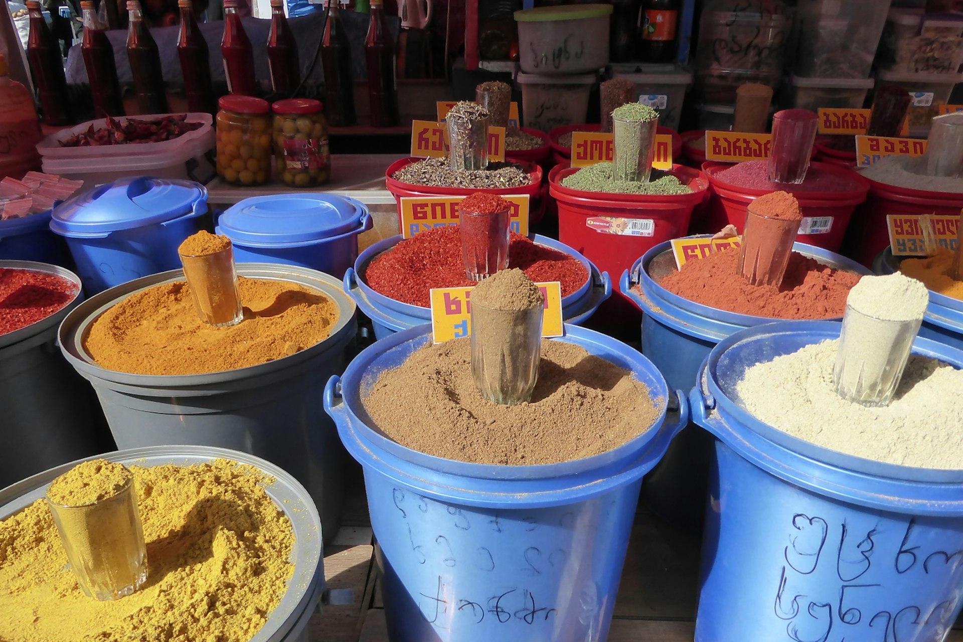 Many large colourful buckets are filled to the brim with different spices of red, brown, beige and yellow