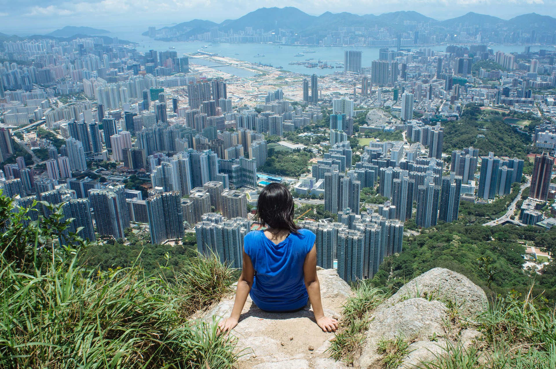 Hiker sits on the way to Lion Rock, part 5 of the MacLeHose trail in Hong Kong. Kowloon and Hong Kong Island are visible from a distance. Hiking is a popular activity among Hong Kong residents and tourists.