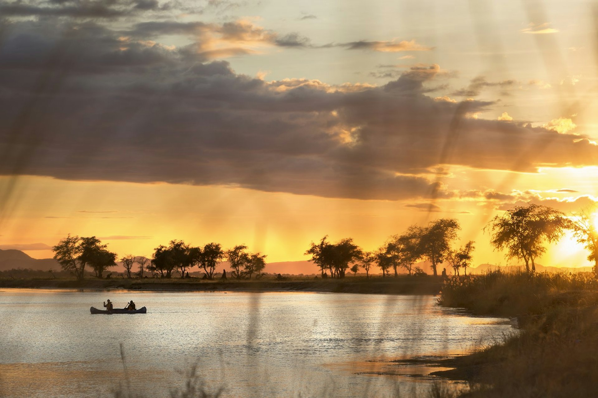 A canoe casts off at dawn from a wild camp on the banks of the Zambezi © Philip Lee Harvey