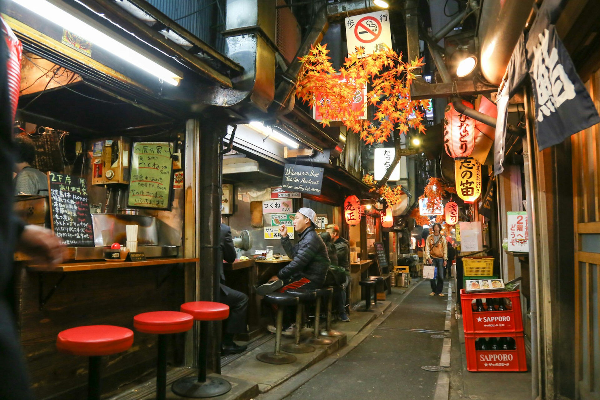 People sit on stools at small stalls along Omoide-yokochō alley