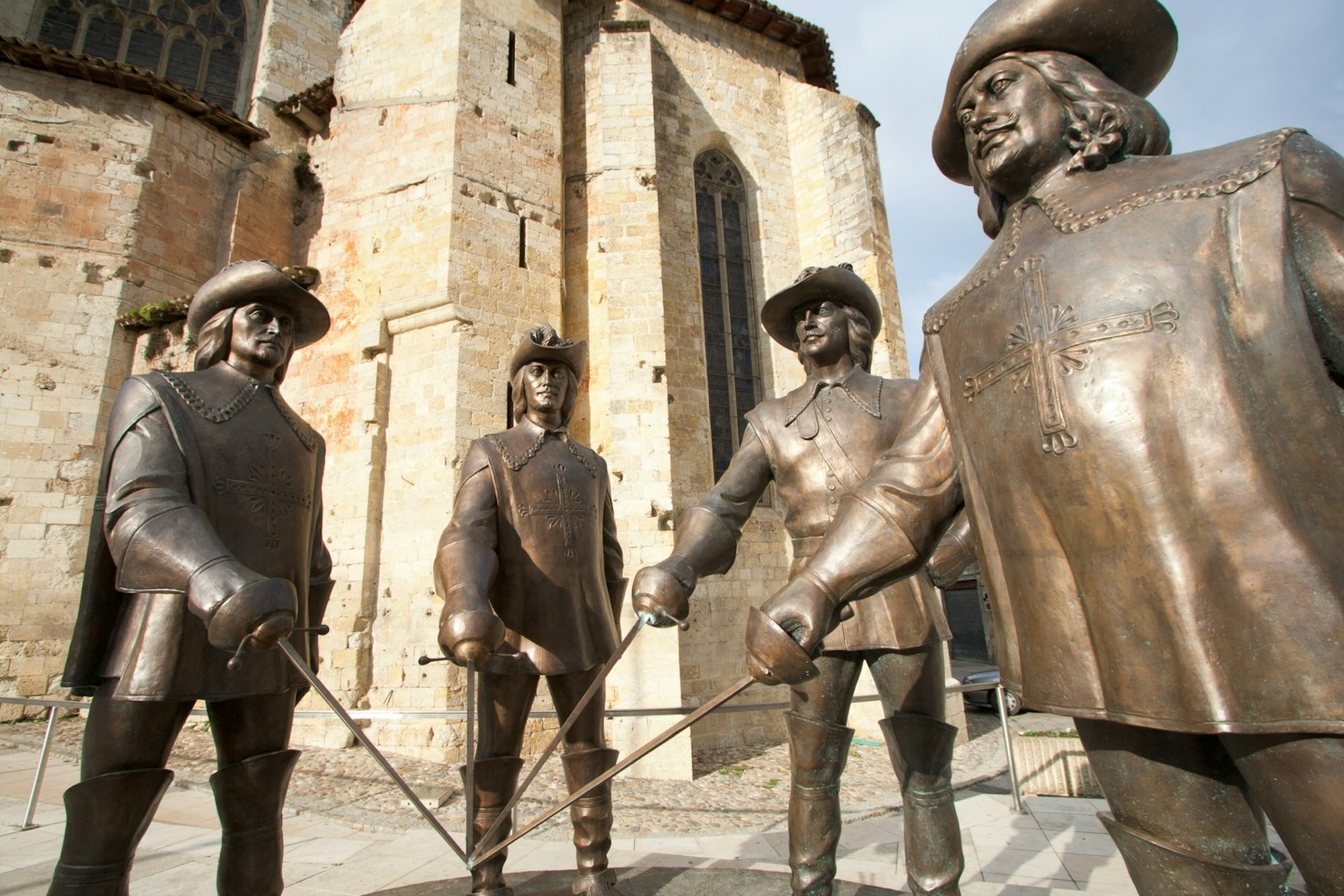 Statues of the musketeers stand guard outside Condom Cathedral, holding their sword blades together. Image © Alain Lauga / Shutterstock