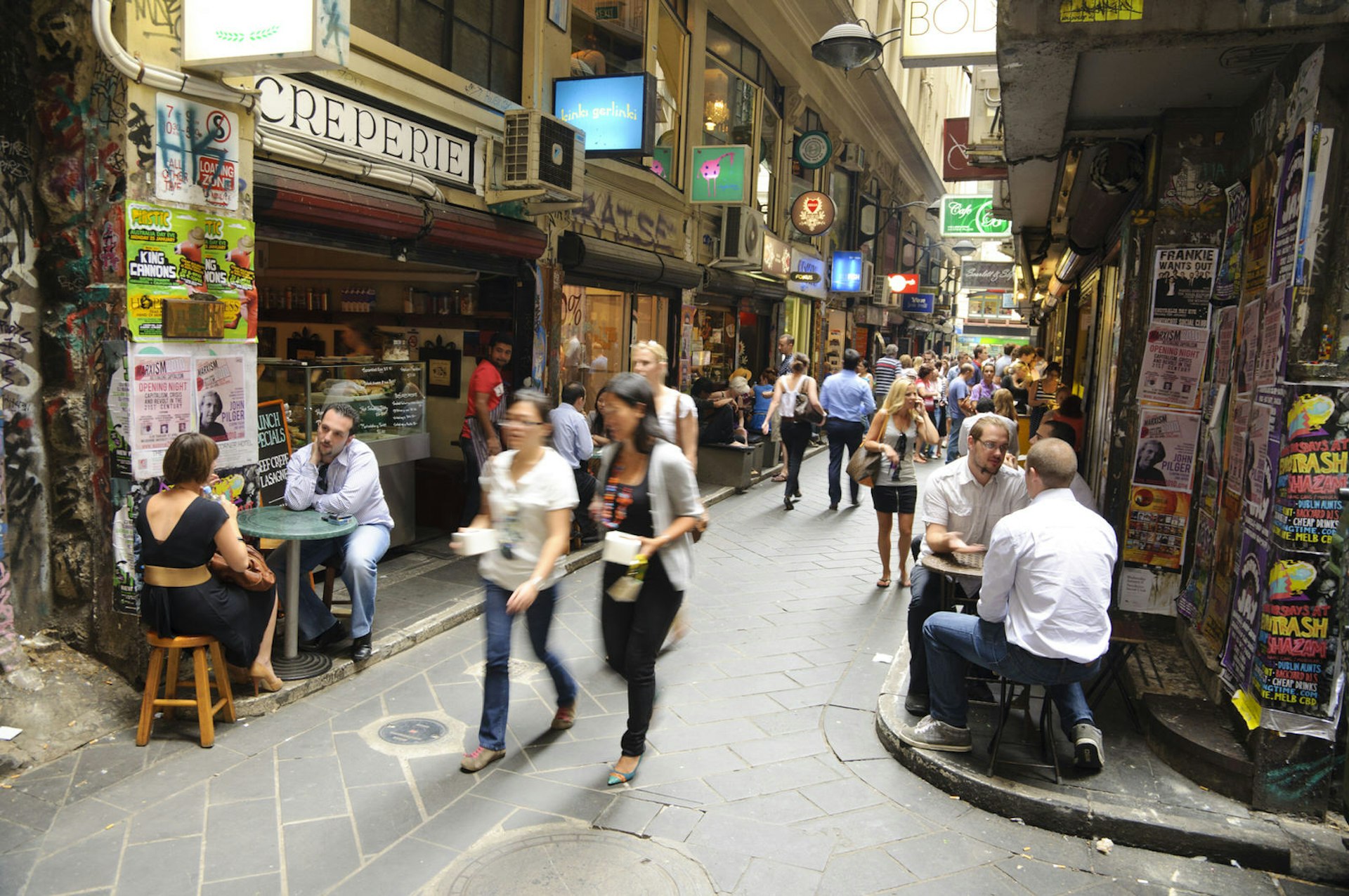 A busy cobbled stone street in Centre Place in Melbourne filled with people walking or sitting outside a shop