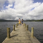 Features - Couple running along the jetty to jump into Lake Windermere, Windermere, Cumbria, England.