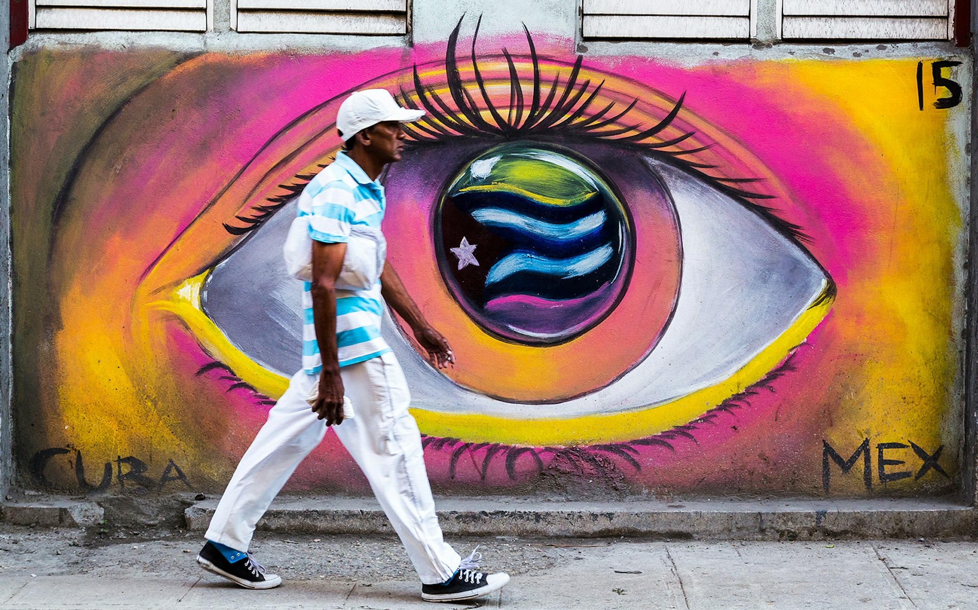 A man walks by a mural of an eye with the Cuban flag in the iris © Wellsie82 / Getty Images 