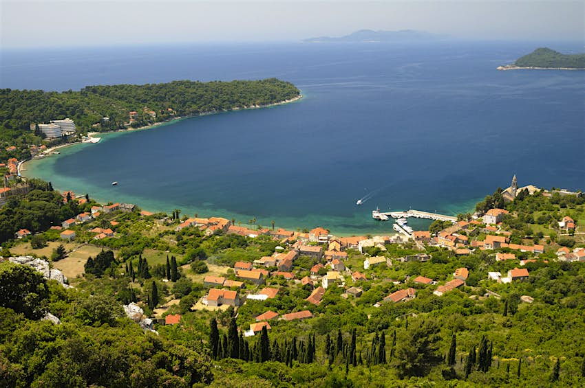 An aerial view over the orange roofs of Lopud; it sits in a beautiful bay, the shore covered in vegetation; out to sea are two tree-lined islands.