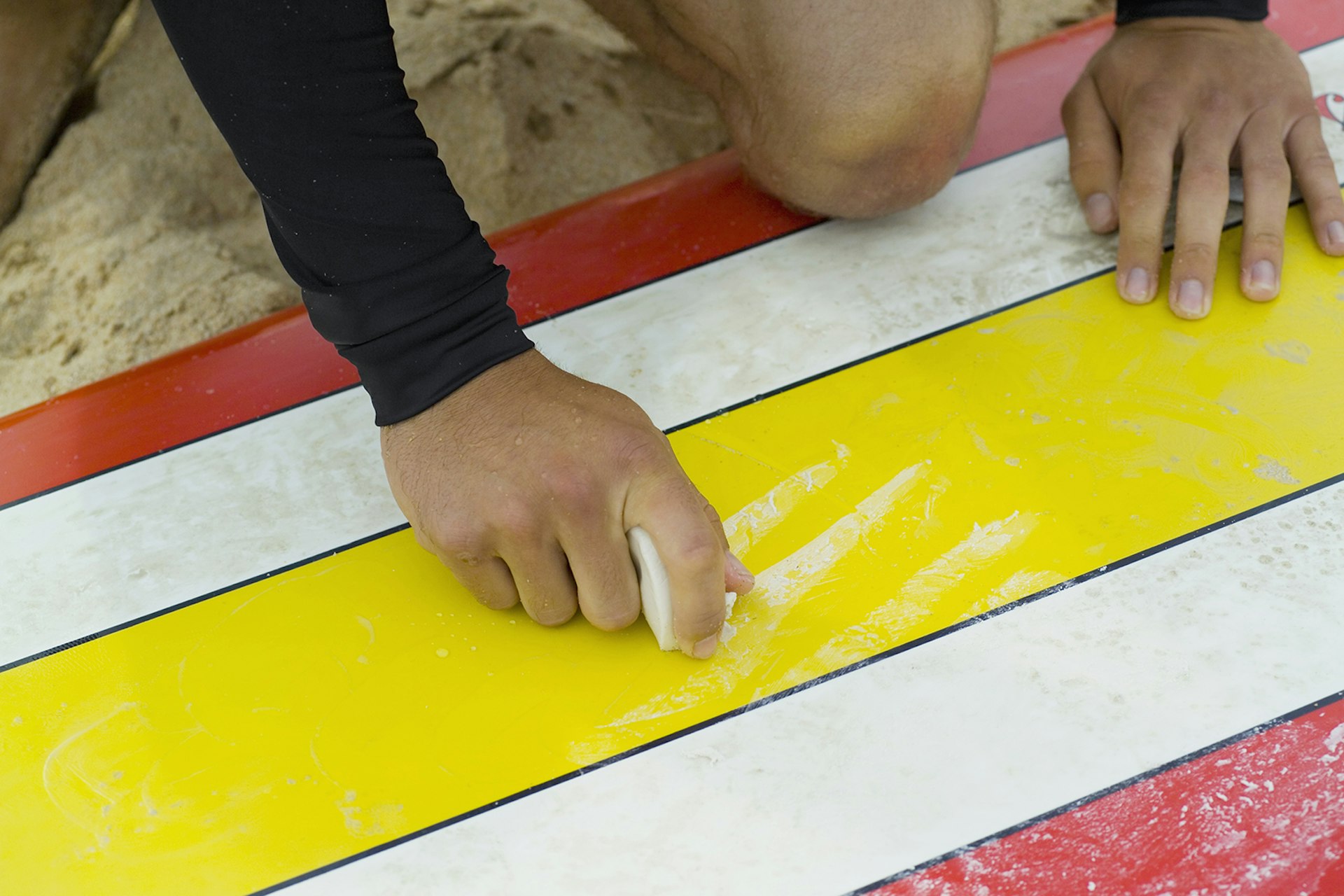 Features - A surfer waxing his surfboard