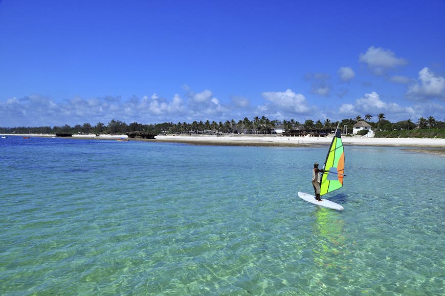 A man on a windsurfing board on clear blue water off the coast of Kenya