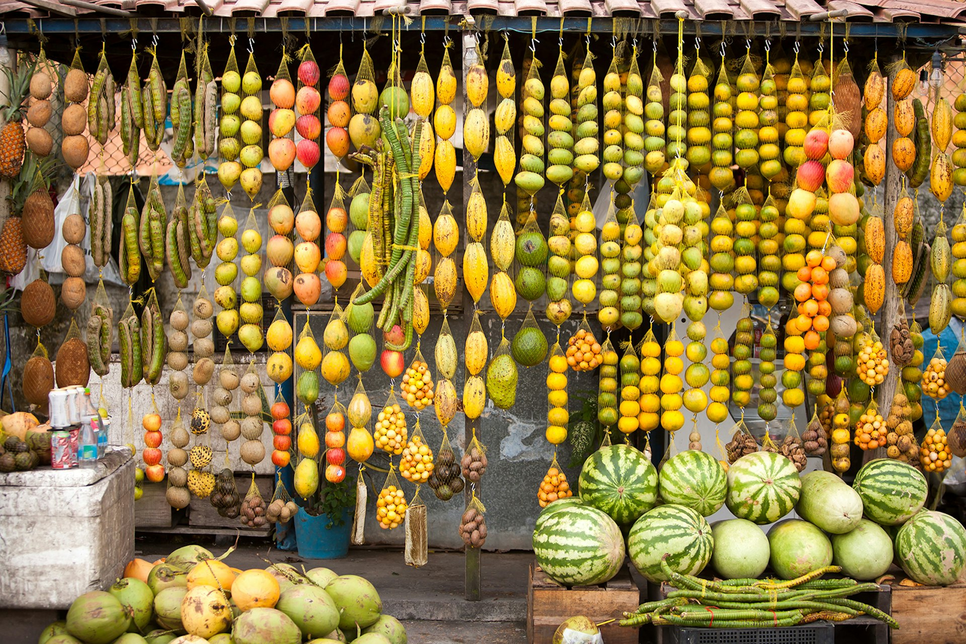 Green, yellow and red fruits hang from the roof of a roadside market in the Amazon. South America.