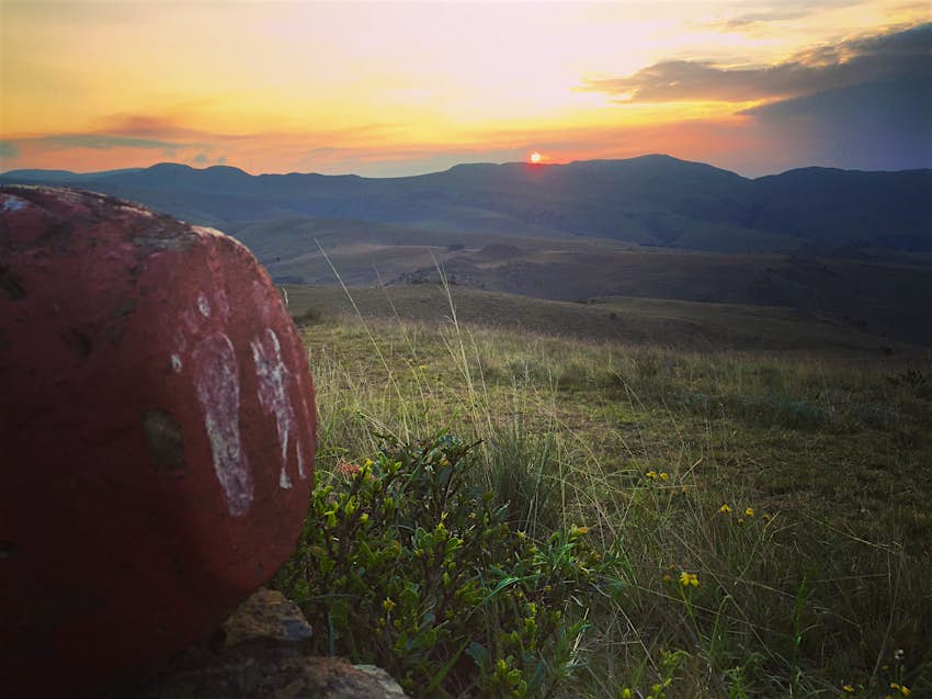Features - IMG_5055-fdcdd507e1c9 Two white human footprints are painted onto a red rock as trail markers within Malolotja Nature Reserve; in the distance is a mountain ridge with the sun just set behind it