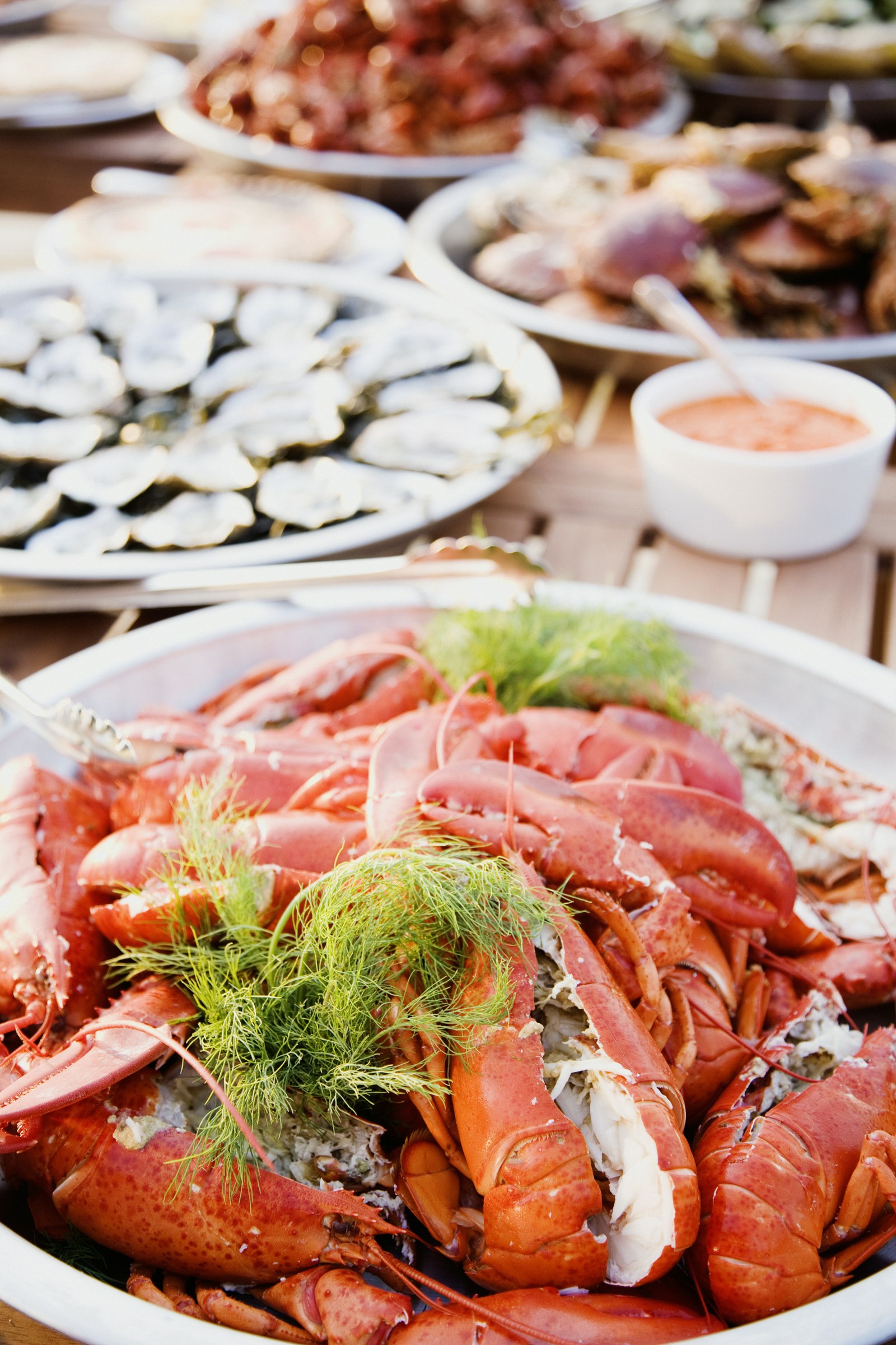 A plate of lobster in the foreground with several other seafood dishes out of focus in the background