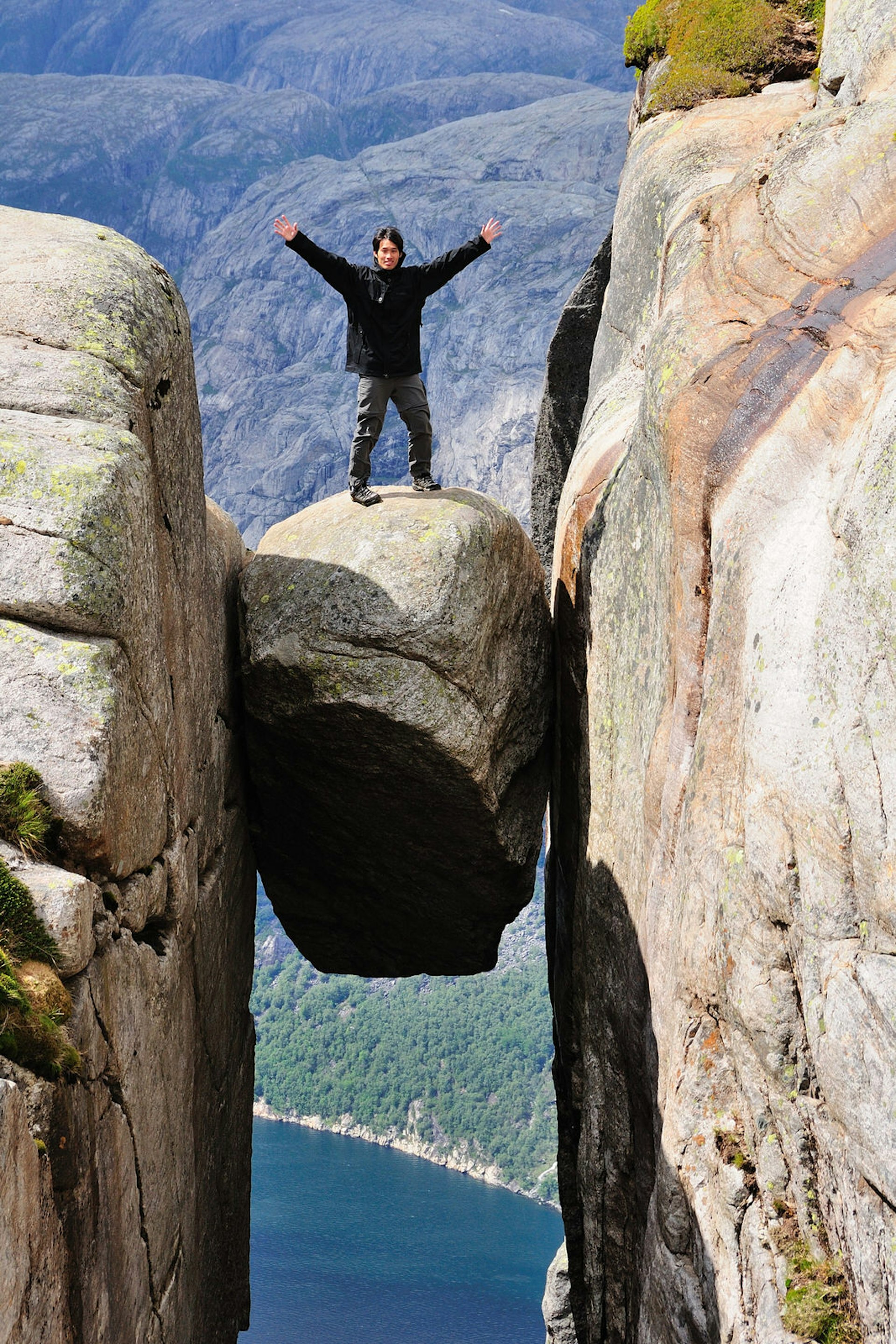 A man posing for a photo on top of the Kjeragbolten, a huge boulder gripped between two cliffs in Norway