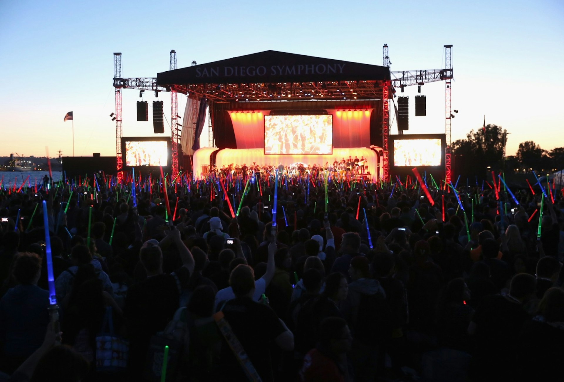 a field of light sabers lights up in front of a stage with musicians and a screen