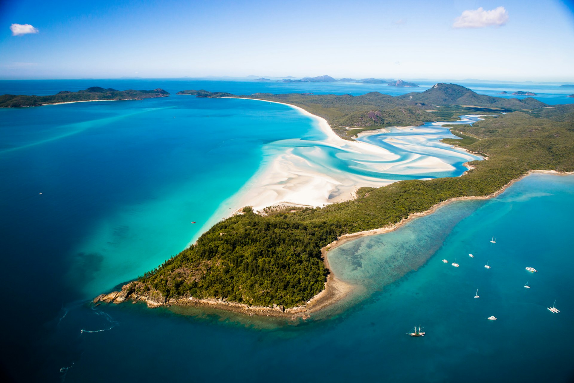 A small peninsula covered in vegetation in the foreground with the turquoise swirls of sea mixing with the white sands at Whitehaven Beach behind