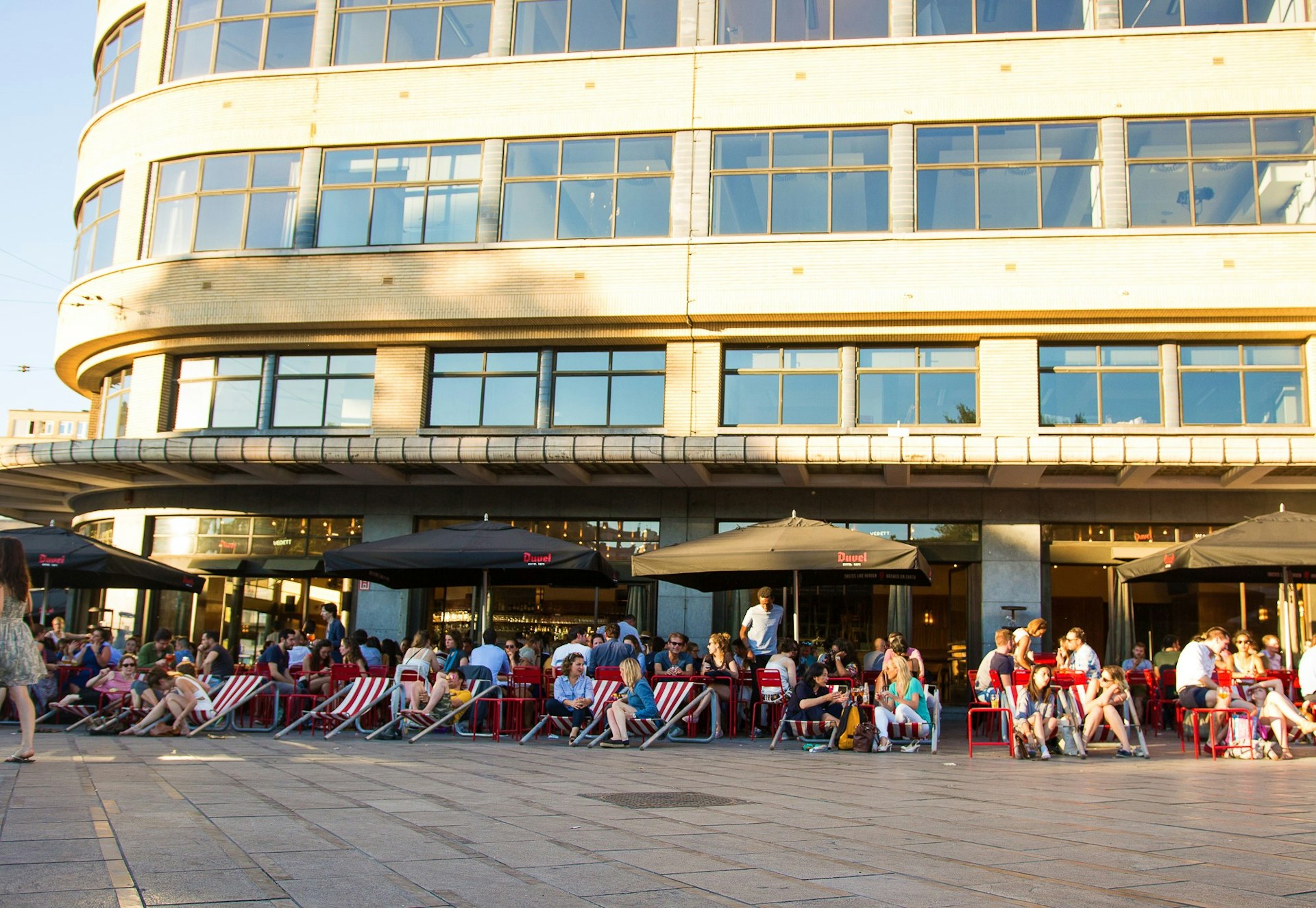 Visitors to Café Belga catch the last of the afternoon sun in their brightly-coloured deckchairs © Analia Glogowski / Lonely Planet