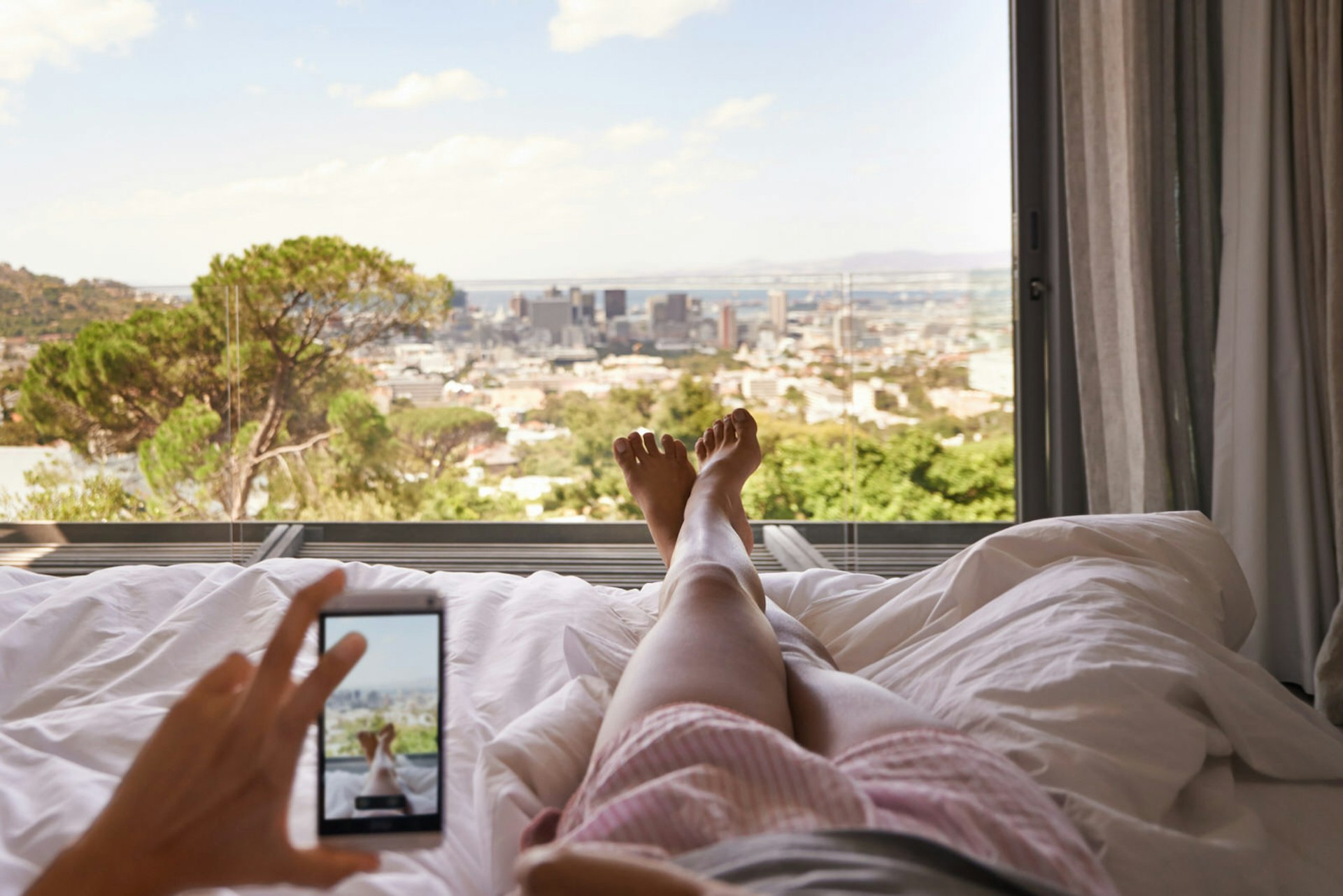 A city view from a bedroom. Person lying on the bed is taking a photo of the view - and their feet