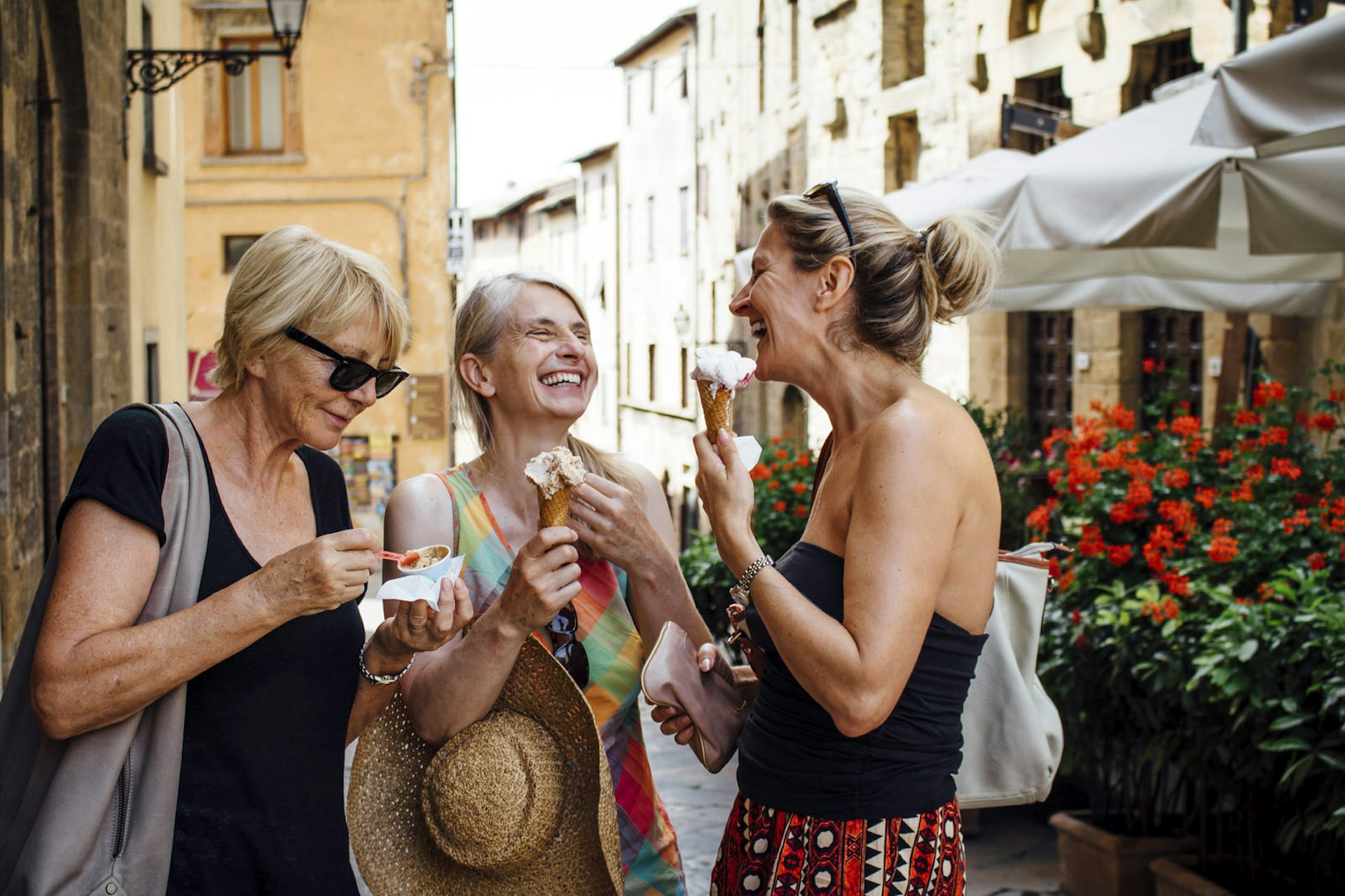 Three women laugh and eat ice cream on a street in Rome.