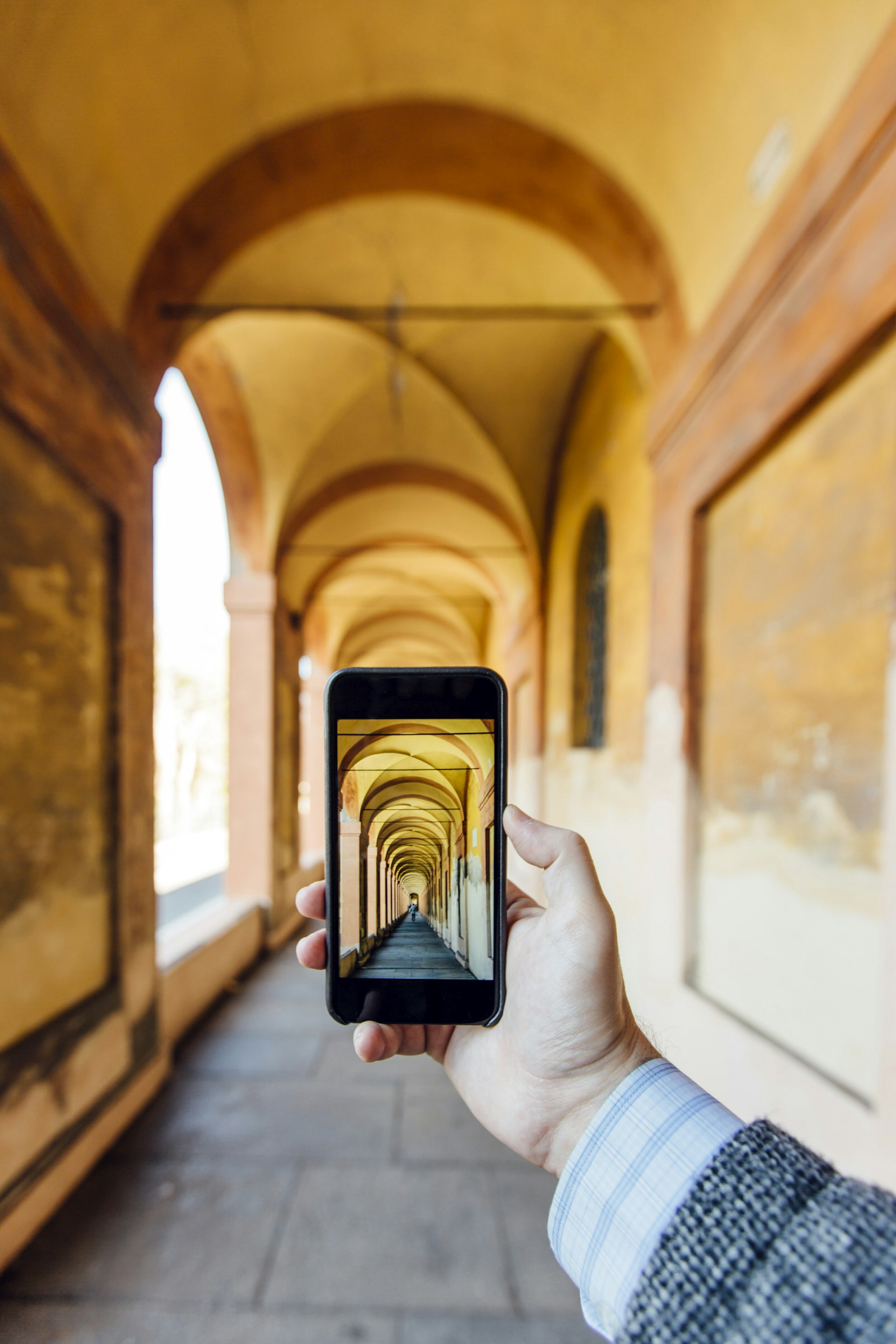 A hand holds an iPhone to take a picture of some old, beautiful archways.