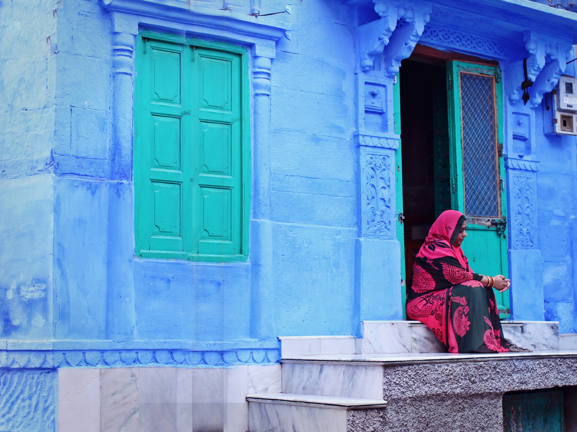 A woman sits in the doorway of a cobalt-blue house in Jodhpur