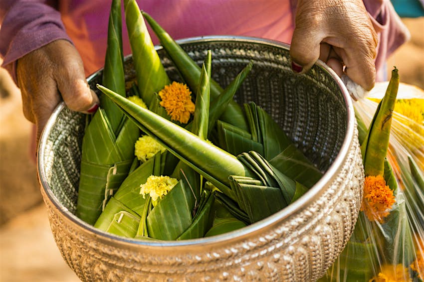 Features - LAO6855_1-cc62df4a1cb1 A woman holds a basket full of marigold offerings