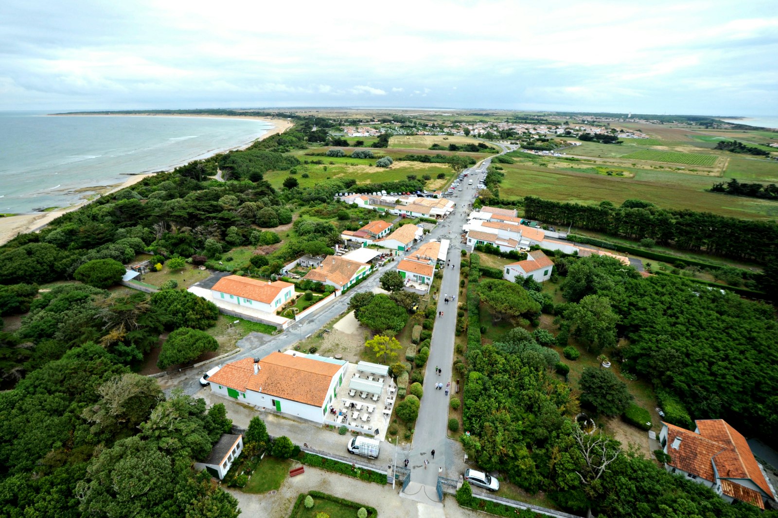 The view from Phare des Baleines lighthouse in Ile de Ré; we see the flat green expanse of the island, studded wityh trees and houses and with a sandy bay curving around the Atlantic Ocean.