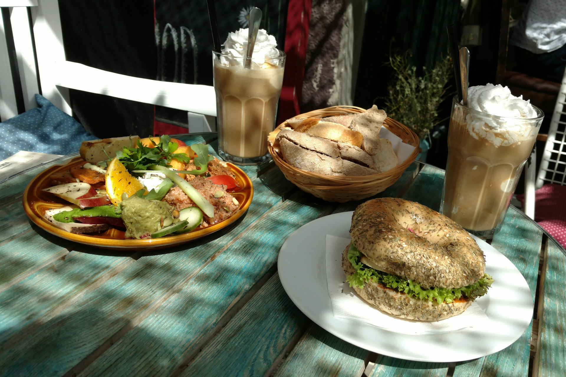 Berlin's best vegan - a colourful salad and bagel sit on a worn, blue wooden table next to two creamy looking coffees at geh Veg in Moabit, Berlin