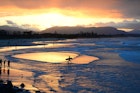 Surfers walk in the shallows as the sun sets on Byron Bay