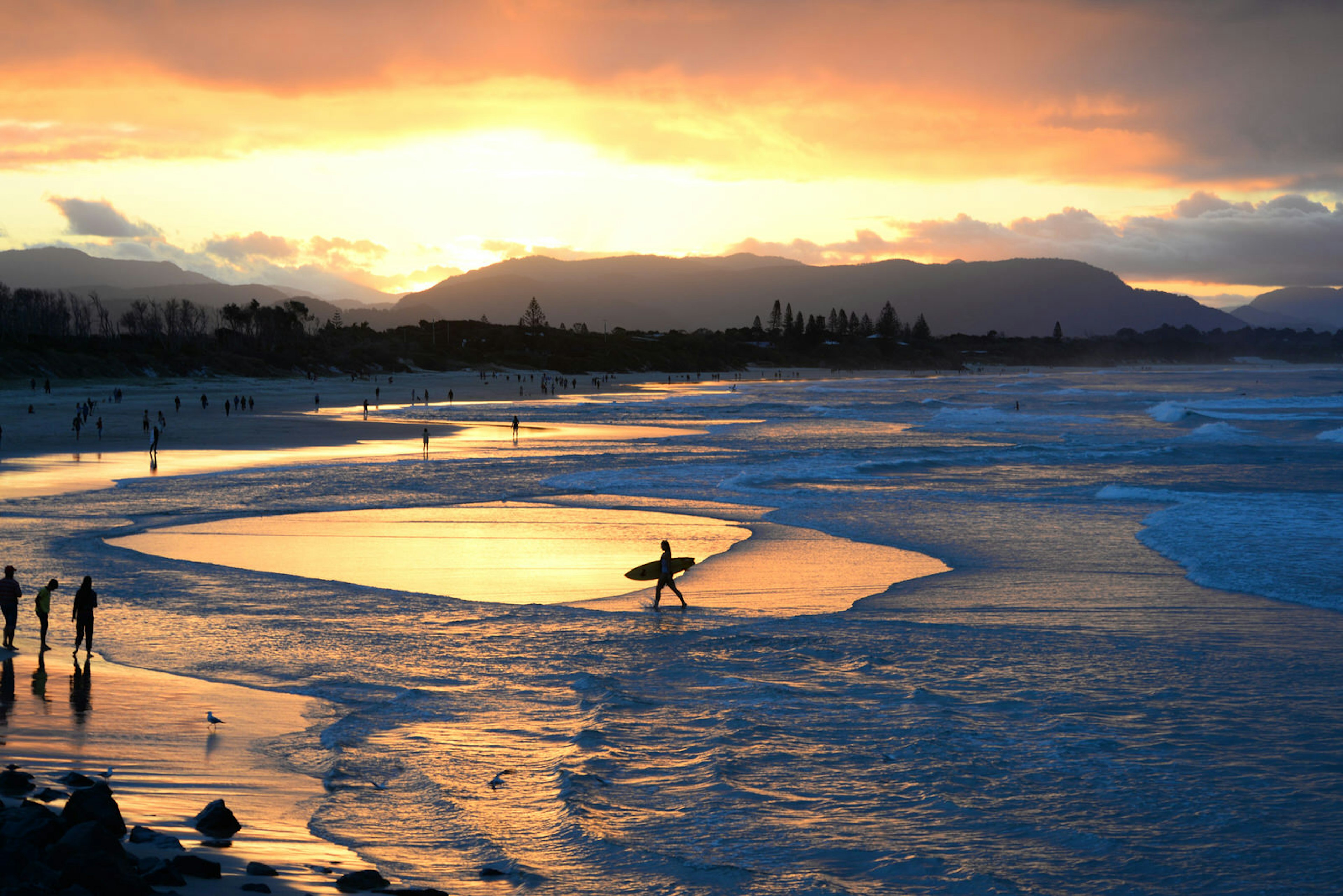 Surfers walk in the shallows as the sun sets on Byron Bay
