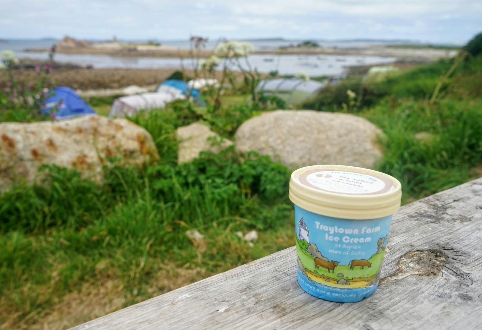 A tub of Troytown Farm ice cream on a picnic bench with the farm's campsite in the background, St Agnes, Isles of Scilly, England, UK © James Kay / Lonely Planet