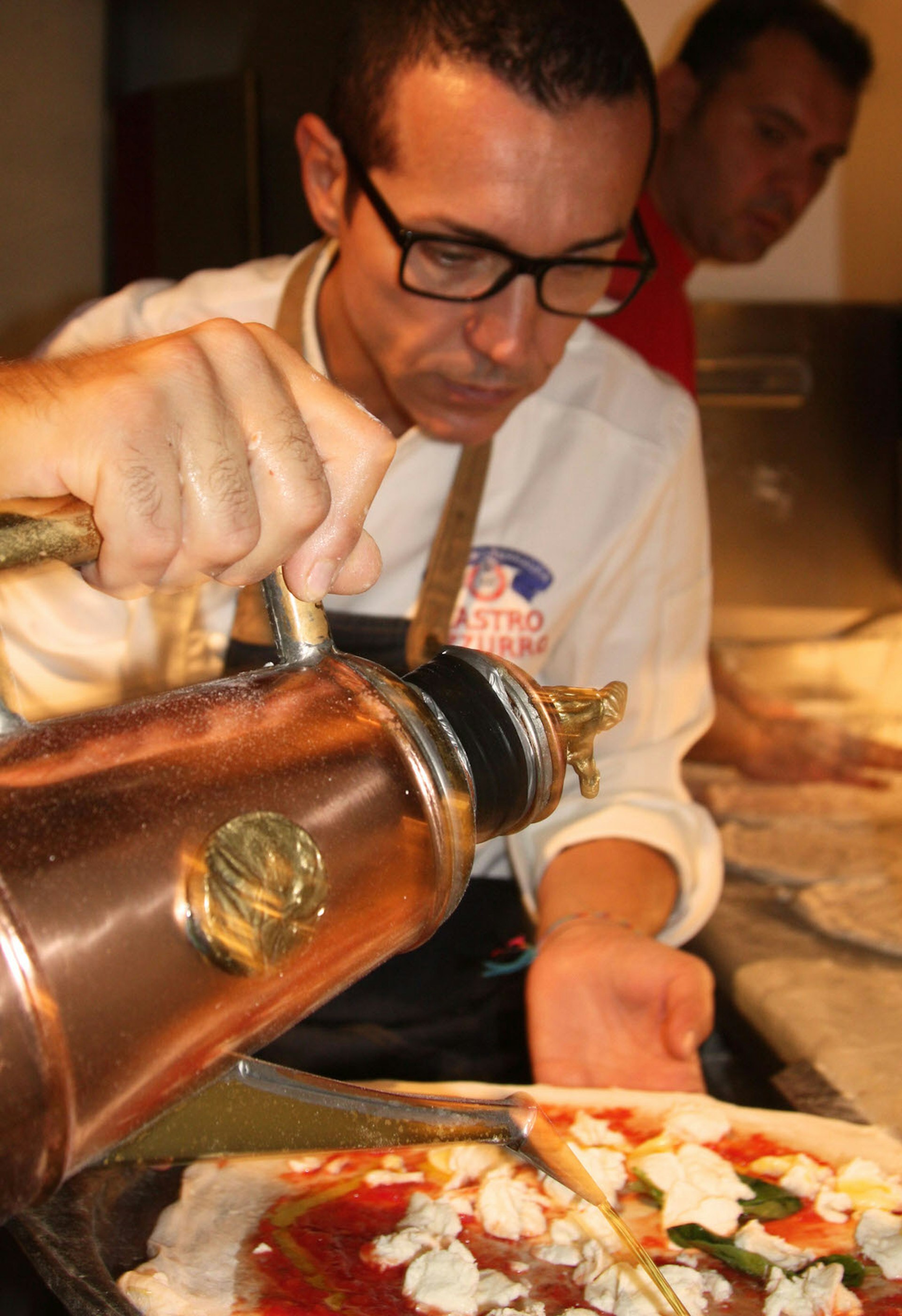 Pizza maestro Gino Sorbillo pours olive oil onto a pizza © Kristin Melia / Lonely Planet