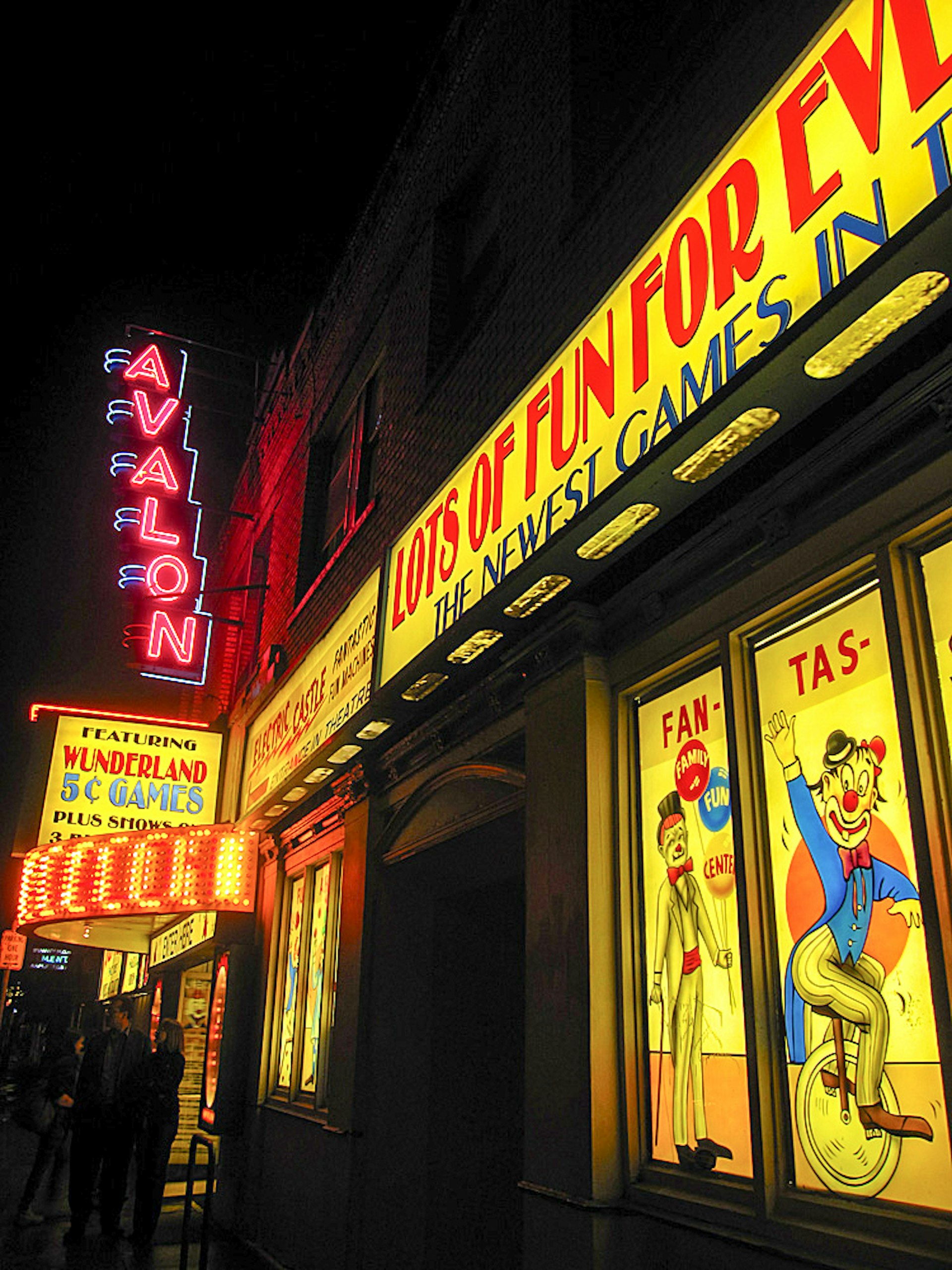 The facade of the Avalon Theater is pictured, with vivid bright yellow and red signs depicting clowns, and neon lights over the door.