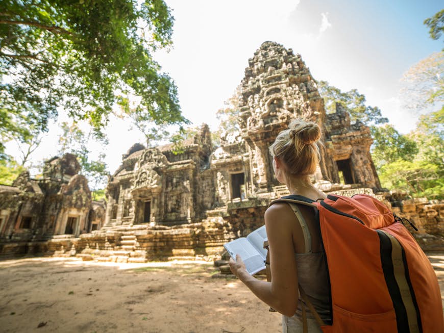 En kvinna som bär en orange ryggsäck utforskar Ta Phrom-templet i Kambodja