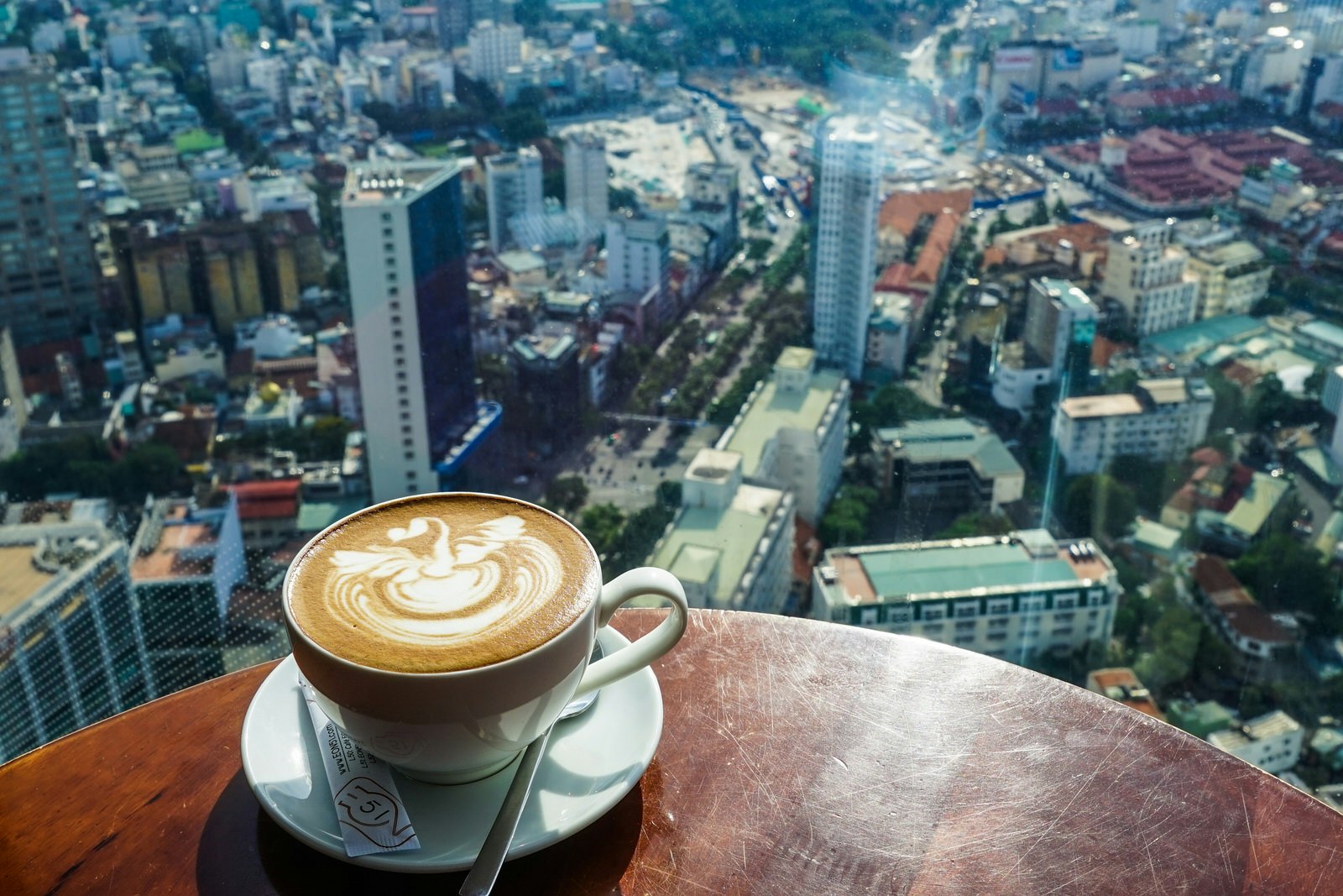 A coffee with a swan drawn in milk perches on a table overlooking Ho Chi Minh City from 50 stories high