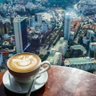A coffee with a swan drawn in milk perches on a table overlooking Ho Chi Minh City from 50 stories high